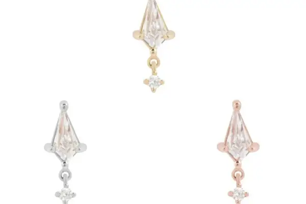 The 14K It’s All Happening earrings come in gold, silver, and rose gold, each with a triangular clear stone and a small round dangling stone, shown against a plain white background.