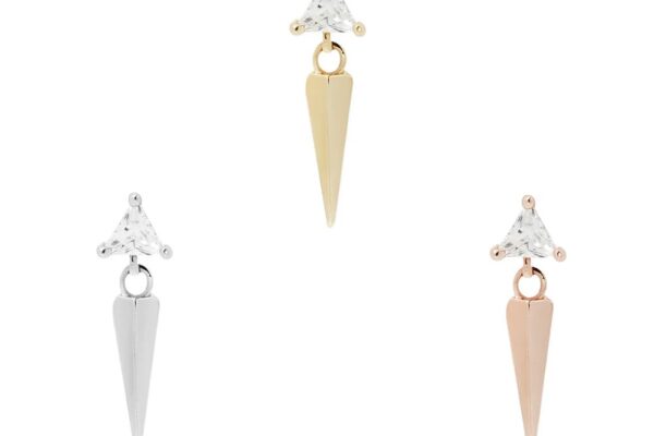 The 14K Saint earrings feature a triangular clear gemstone atop a pointed metal drop, shown in silver, gold, and rose gold tones on a plain white background.