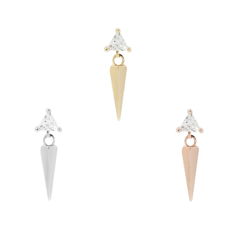 The 14K Saint earrings feature a triangular clear gemstone atop a pointed metal drop, shown in silver, gold, and rose gold tones on a plain white background.