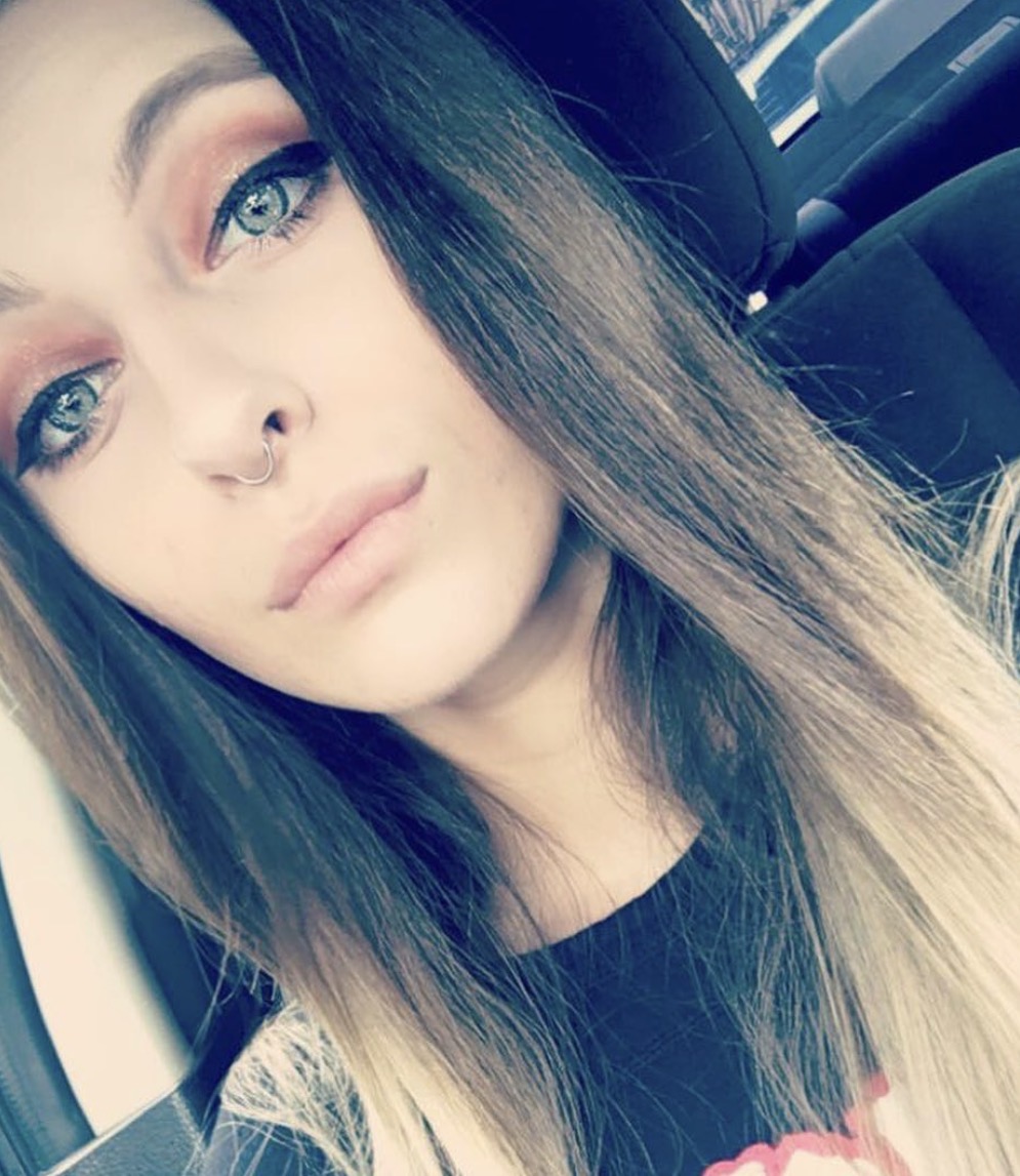 A young woman with long brown and blonde hair, wearing a black shirt, bold eye makeup, and a Seam Ring – Niobium – 18G nose ring, sits in the car’s driver seat looking into the camera with a neutral expression. A young woman with long brown and blonde hair, wearing a black shirt, bold eye makeup, and a Seam Ring – Niobium – 18G nose ring, sits in the car’s driver seat looking into the camera with a neutral expression.