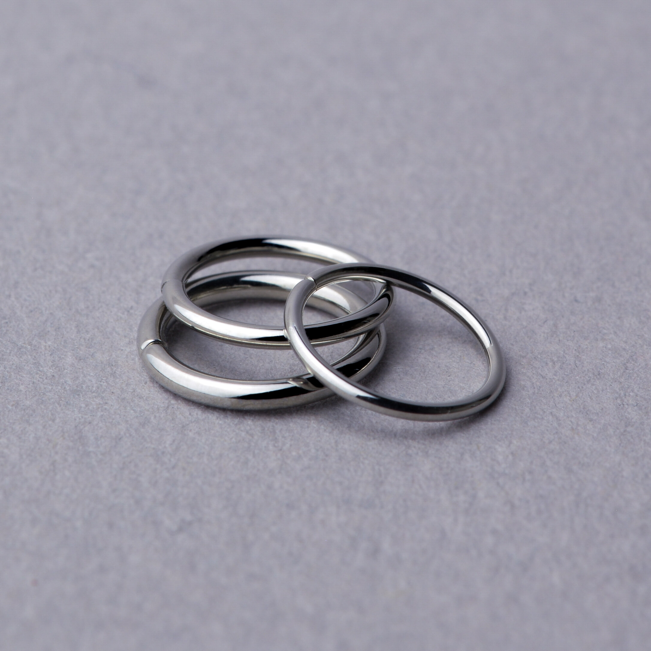 Three Seam Ring – Niobium – 18G pieces are stacked together on a light gray surface. Three Seam Ring – Niobium – 18G pieces are stacked together on a light gray surface.