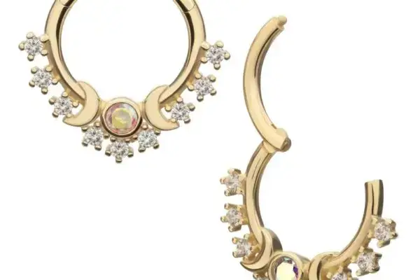 A pair of gold septum rings featuring a central iridescent gem and clusters of small clear crystals in an ornate design. One is closed; the other, the 14K Triple Moon Clicker, is open to display its clasp.