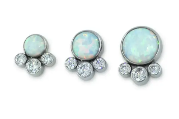 Three Bezel Set Cabochon Cluster - Tangent earrings, each with a round opal cabochon atop three clear gemstones in a tangent row, are displayed on a white background.