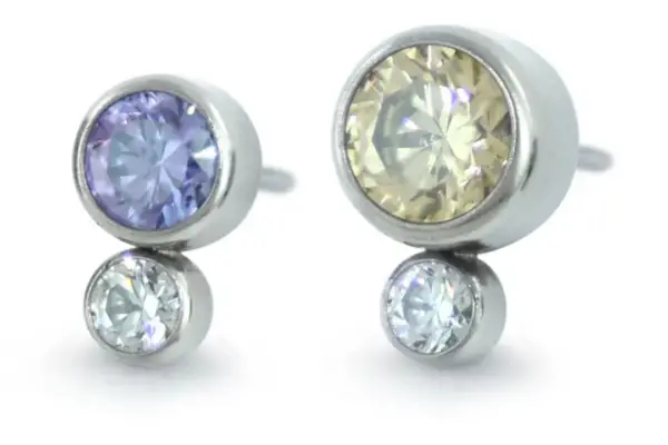 The Bezel Set Two Gem Cluster stud earrings in silver feature mismatched large yellow and purple gemstones, each paired with a small clear gem for a unique, modern style.