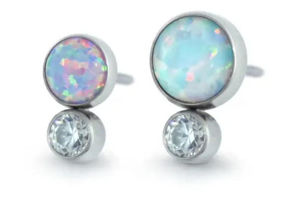 A pair of stud earrings inspired by the Bezel Set Two Gem Cabochon Cluster, featuring round opal cabochons above clear gemstones in silver settings.