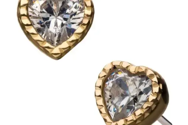 Two 14K Beaded Gem Heart stud earrings, gold and heart-shaped with clear faceted center gemstones, are shown against a white background.