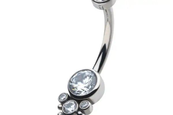 The Beaded Terraced Cluster is a titanium navel curve with a silver finish, showcasing a large central clear gemstone, surrounded by smaller clear gems and an extra clear gem on the opposite end.