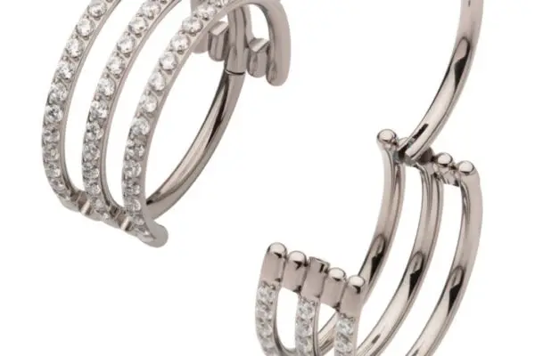 The Triple Gem Row Clicker features a trio of silver bands, each set with sparkling white stones, inspired by modern elegance. Its stylish design is showcased against a clean white background.