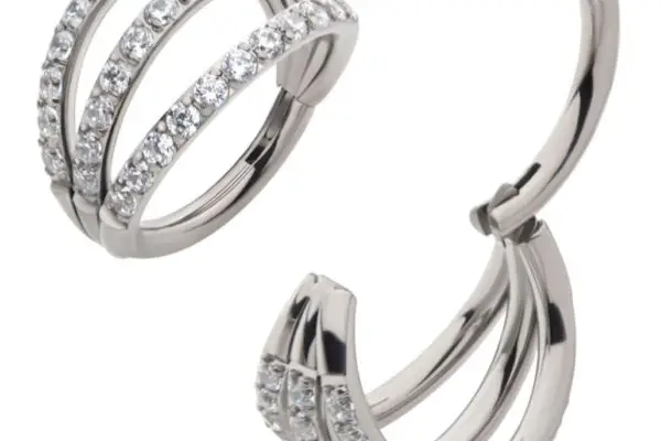 The Triple Hoop Clicker earrings feature three silver hoops adorned with clear, sparkling gemstones. Displayed on a white background, one earring is closed while the other is open to show the clasp mechanism.