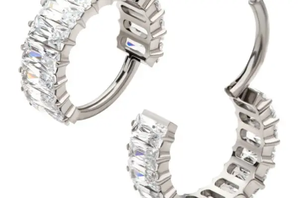 The Baguette Side Clicker showcases silver titanium hoop earrings, each adorned with rectangular clear gemstones set side by side along the outer edge, displayed against a white background.