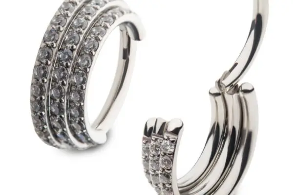 The Triple Stacked Gem Clicker features silver titanium hoops with three rows of small, round clear gemstones, shown from the front and side to showcase their polished shine and intricate design.