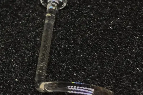 A small, clear Nostril Screw Glass Retainer - Left with a flat circular end is displayed on a textured black surface.