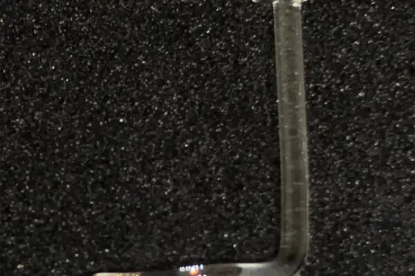 A small, transparent Nostril Screw Glass Retainer - Right with a rounded end and L-shape rests discreetly on a textured black surface.