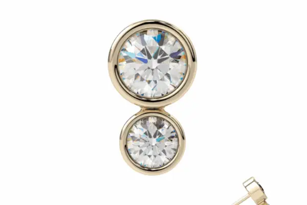 The 14K Double Bezel gold stud earring features two round, clear gemstones stacked vertically with a post and butterfly backing, displayed on a white background.