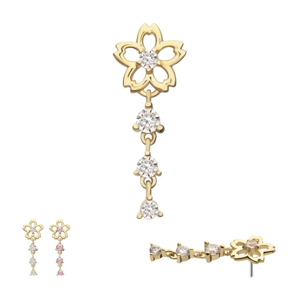 The 14K Cherry Blossom Flower Dangle showcases a delicate flower design with three round gems on a dangling chain. The main image displays white stones, with pink and white options below and a side view at the bottom right.