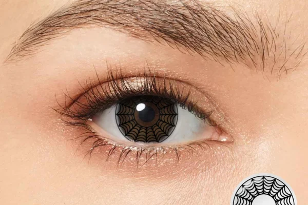 A close-up of a person's eye wearing Magister - White Spider Web contacts featuring a bold black web pattern—ideal for Halloween. An inset displays the lens: a clear circle with an intricate black spiderweb over the iris.