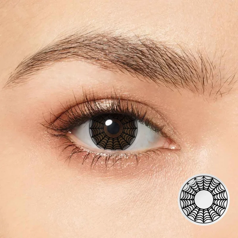 A close-up of a person's eye wearing Magister - White Spider Web contacts featuring a bold black web pattern—ideal for Halloween. An inset displays the lens: a clear circle with an intricate black spiderweb over the iris.
