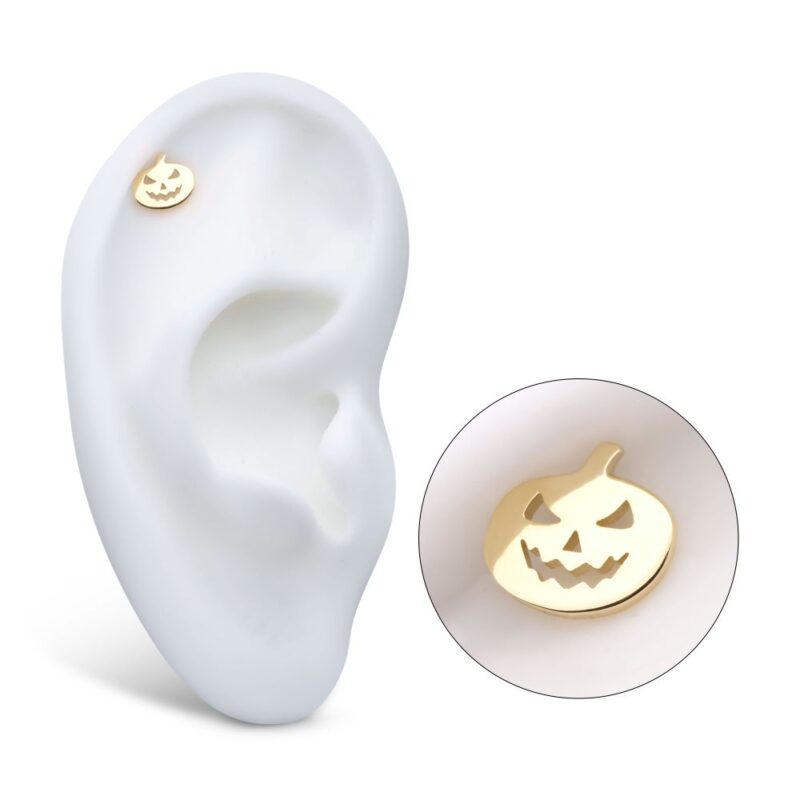 The 14K Jack-o-lantern Cut Out earring, shaped like a gold pumpkin with a carved jack-o’-lantern face, is displayed on a white ear model, with a close-up inset showcasing its intricate details.