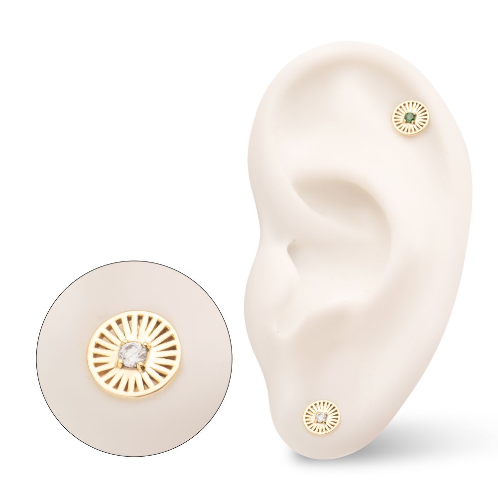 The 14K Radiant Circle with Gem, a gold circular stud earring with a sunburst design and clear gemstone center, is displayed on a model ear. An inset highlights the earring’s intricate details up close. The 14K Radiant Circle with Gem, a gold circular stud earring with a sunburst design and clear gemstone center, is displayed on a model ear. An inset highlights the earring’s intricate details up close.