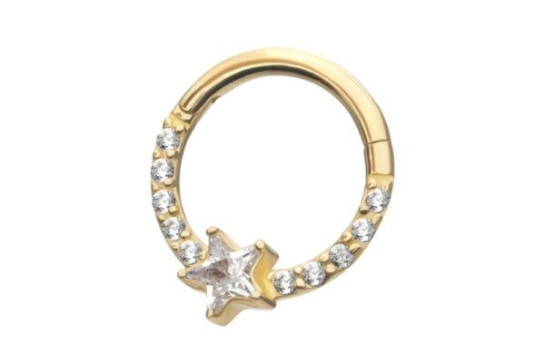 The 14K Star Shine Clicker is a gold hoop earring embellished with small clear gemstones and a star-shaped gem at the bottom center.