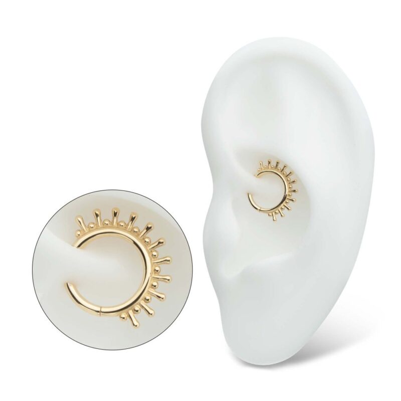 The 14K 11 Spiked Clicker, a gold hoop cartilage earring with a spiked sunburst design, is shown inserted into a white model ear. A close-up view highlights the details of its decorative pattern.