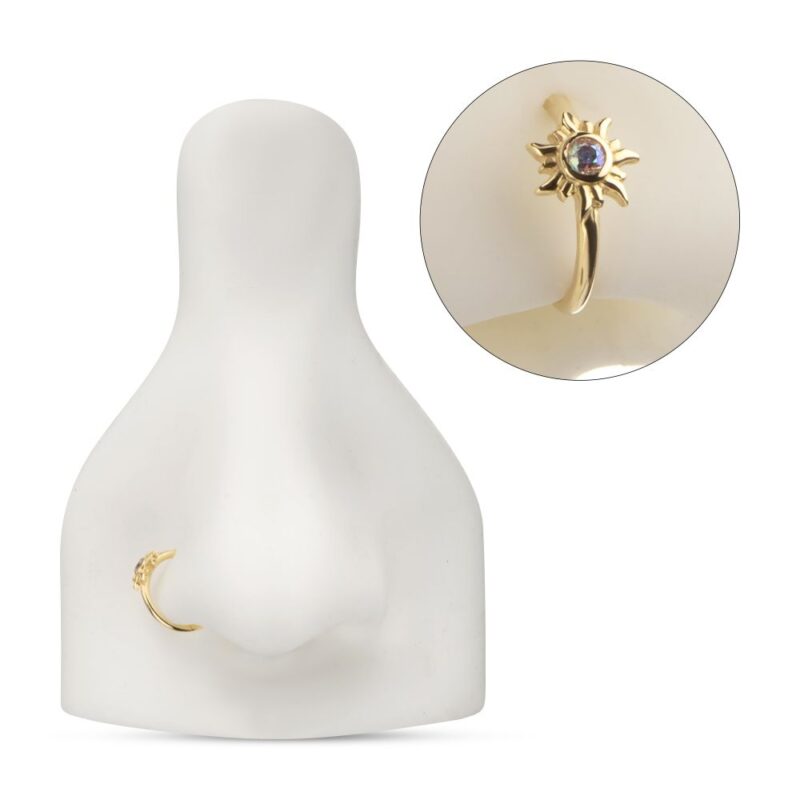 A 14K Sunburst Side Clicker is displayed on a white nose stand, featuring a flower-inspired design with a central gemstone. An inset shows close-up details of the intricate sunburst pattern and the gemstone’s color.