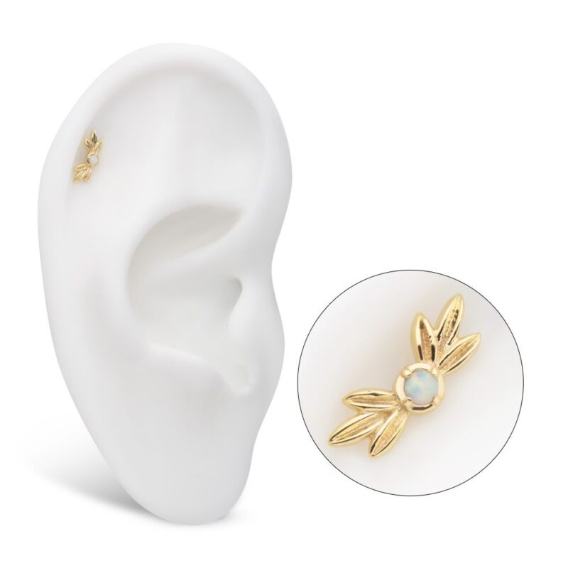 The 14K Triple Leaf is a small gold stud earring featuring a light gemstone and leaf-like design, displayed on a white ear model. A close-up inset highlights its intricate details.