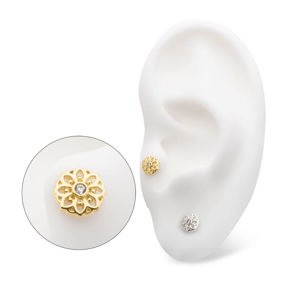 A white ear model displays two stud earrings: the 14K Mandala Flower gold floral stud with a central gemstone on the upper ear, and a silver floral stud with a gemstone on the lower ear. An enlarged view highlights the gold stud’s intricate design. A white ear model displays two stud earrings: the 14K Mandala Flower gold floral stud with a central gemstone on the upper ear, and a silver floral stud with a gemstone on the lower ear. An enlarged view highlights the gold stud’s intricate design.