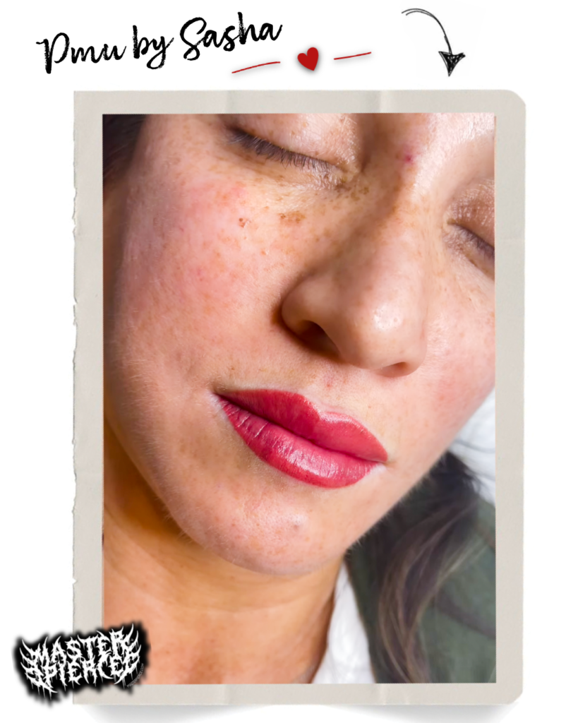 A person with closed eyes shows fresh red lip permanent makeup. Freckles are visible on their face, and the words "Pmu by Sasha" appear at the top of the image with a small red heart. Meet Kri Percing Artist, whose artistry enhances natural beauty in every detail.