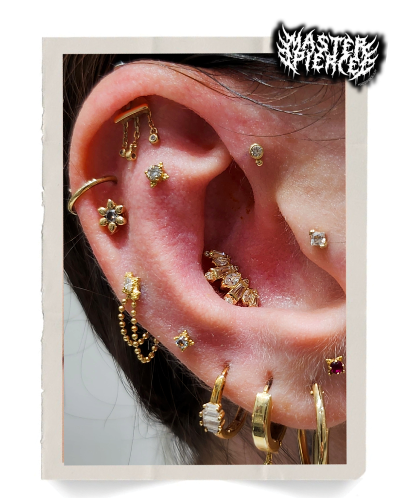 A close-up of an ear adorned with multiple gold earrings, studs, and hoops in various shapes and sizes, including floral and gem designs.