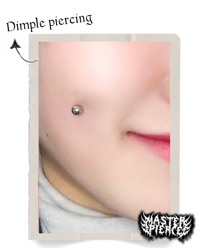Close-up of a person’s cheek with a dimple piercing, labeled “Dimple piercing” with an arrow pointing to the piercing. The person has light skin and is smiling slightly—an eye-catching detail featured in the Ultimate Guide to Advanced Piercings.