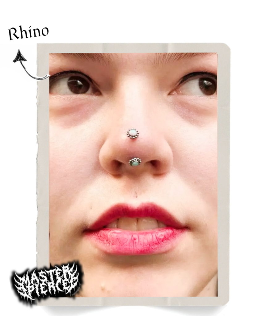 Close-up of a persons face with two nose piercings—a septum ring and a vertical piercing through the tip. An arrow labeled Rhino points to the vertical piercing. The person has pink lipstick.
