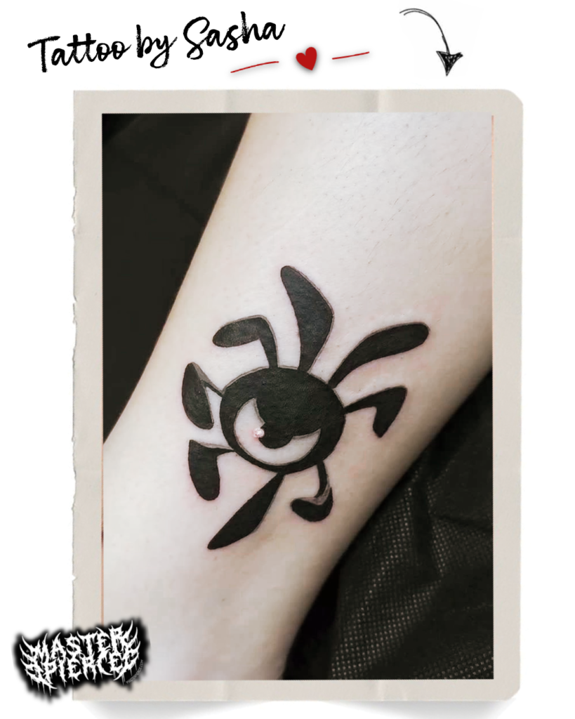 A bold black abstract spider tattoo with a crescent moon on a forearm. The design features curved lines for legs and Tattoo by Sasha is written above with a small heart and arrow.