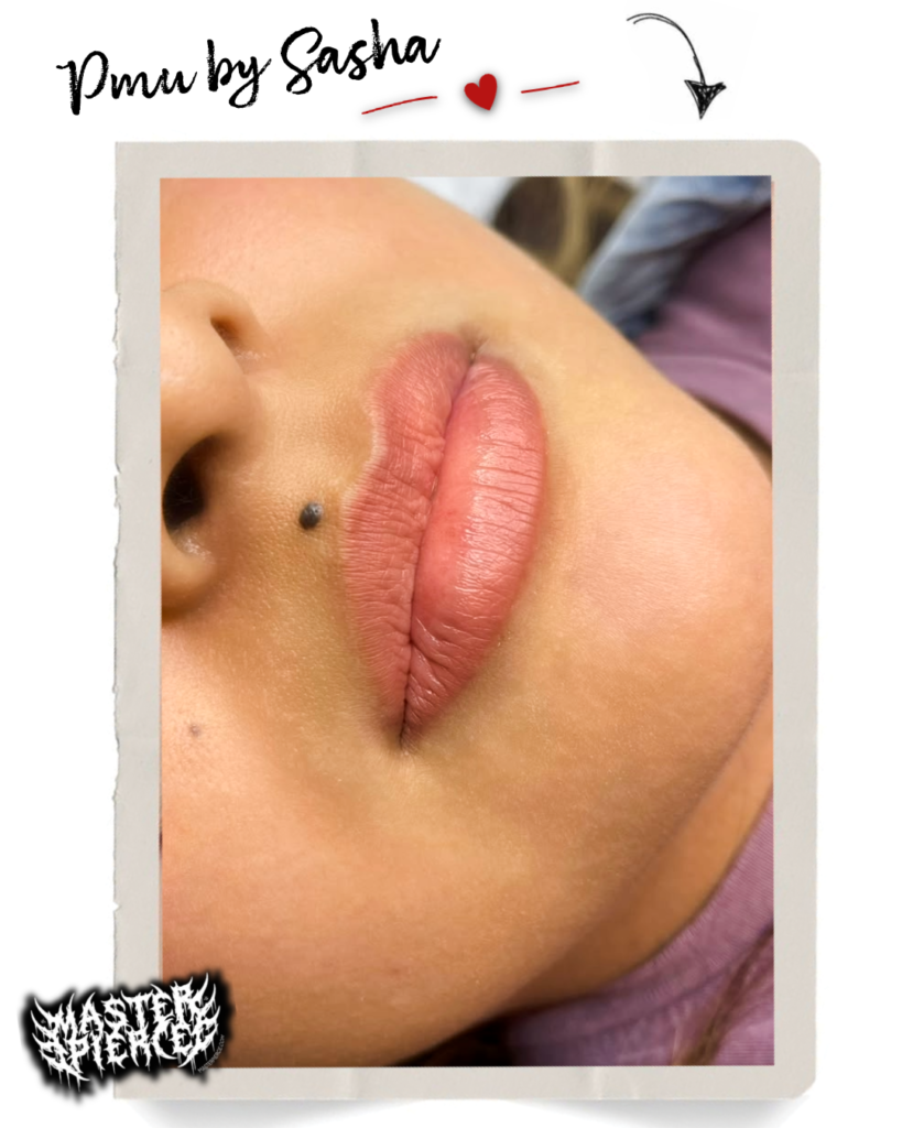 Close-up of a persons lips with soft, natural-looking pink lip color. The text Pmu by Sasha and a heart graphic are at the top. There is a small beauty mark above the upper lip.